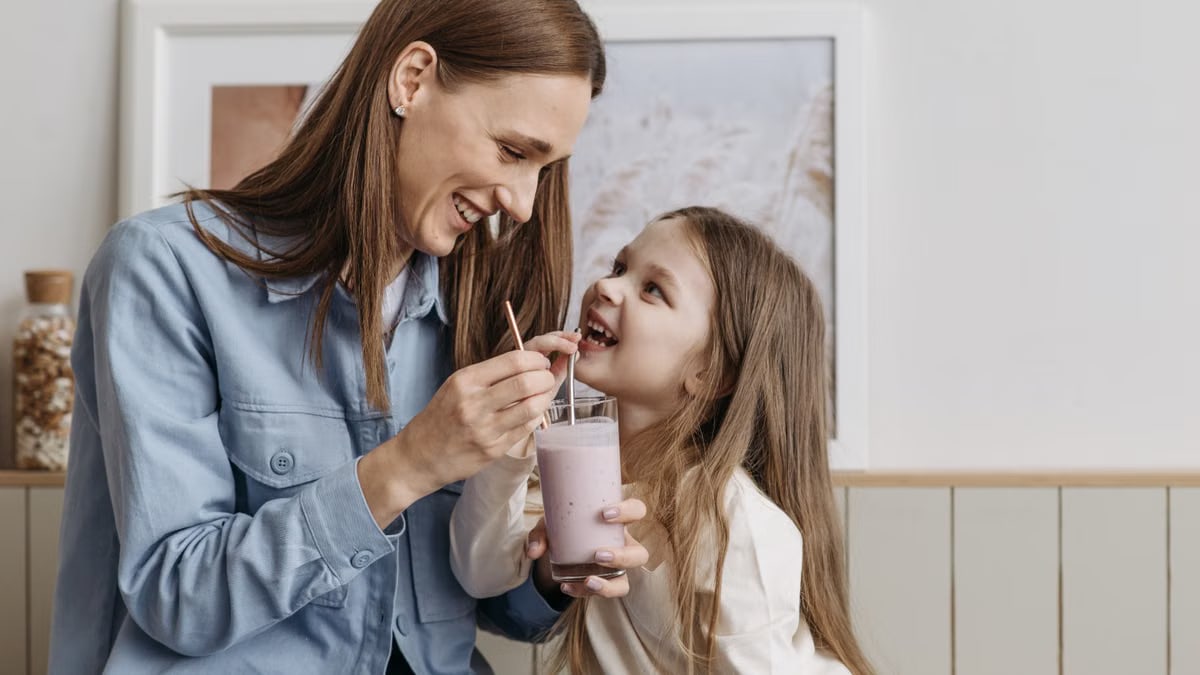 A joyful moment of a mother and daughter sharing a strawberry milkshake indoors.